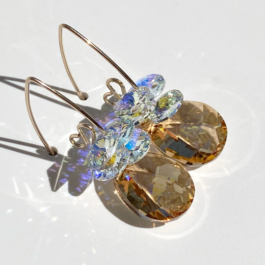 A pair of elegant scroll design crystal earrings with faceted pear cut crystals in golden and merlot colors, displayed on a white background.